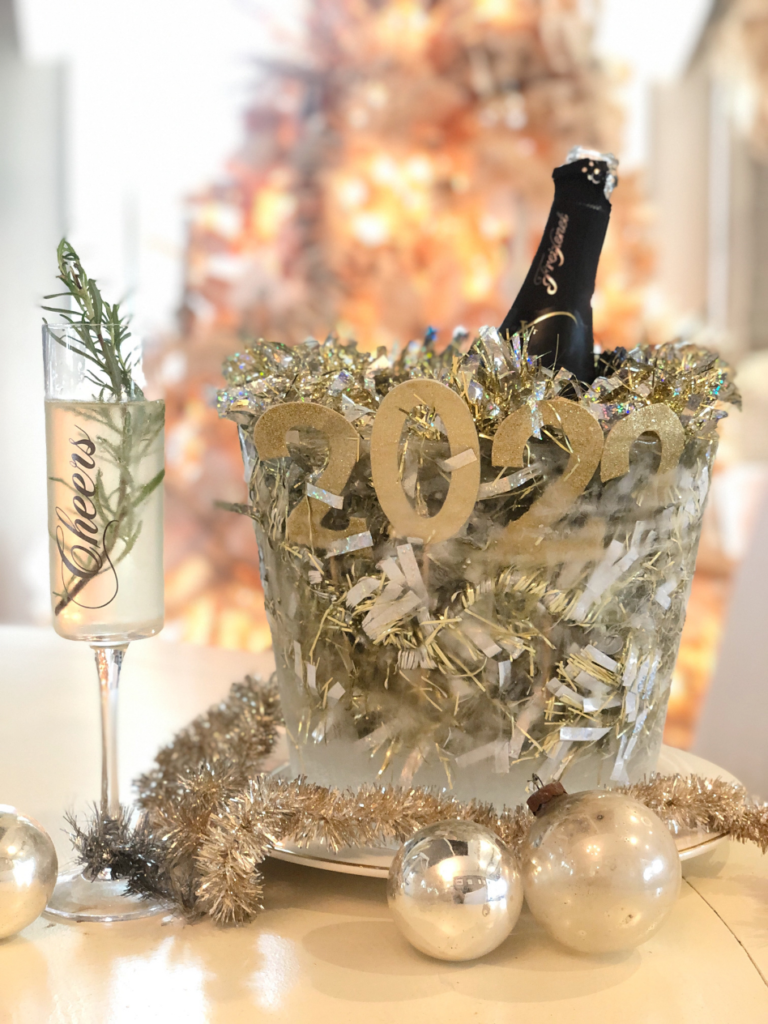 decorative ice bucket with gold/silver tinsel and gold glitter numbers 2022 frozen inside the ice and bottle of prosecco inside the ice bucket