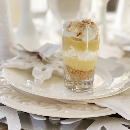 coconut pie mini parfait in clear glass vintage juice glass standing on top of layered white plates with snowflake ornament in background