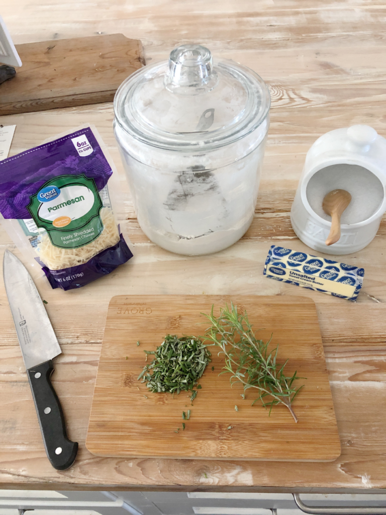 ingredients for parmesan rosemary shortbread crackers bag of grated parmesan cheese cannister of flour jar of kosher salt stick of butter chopped rosemary on cutting board with large knife beside