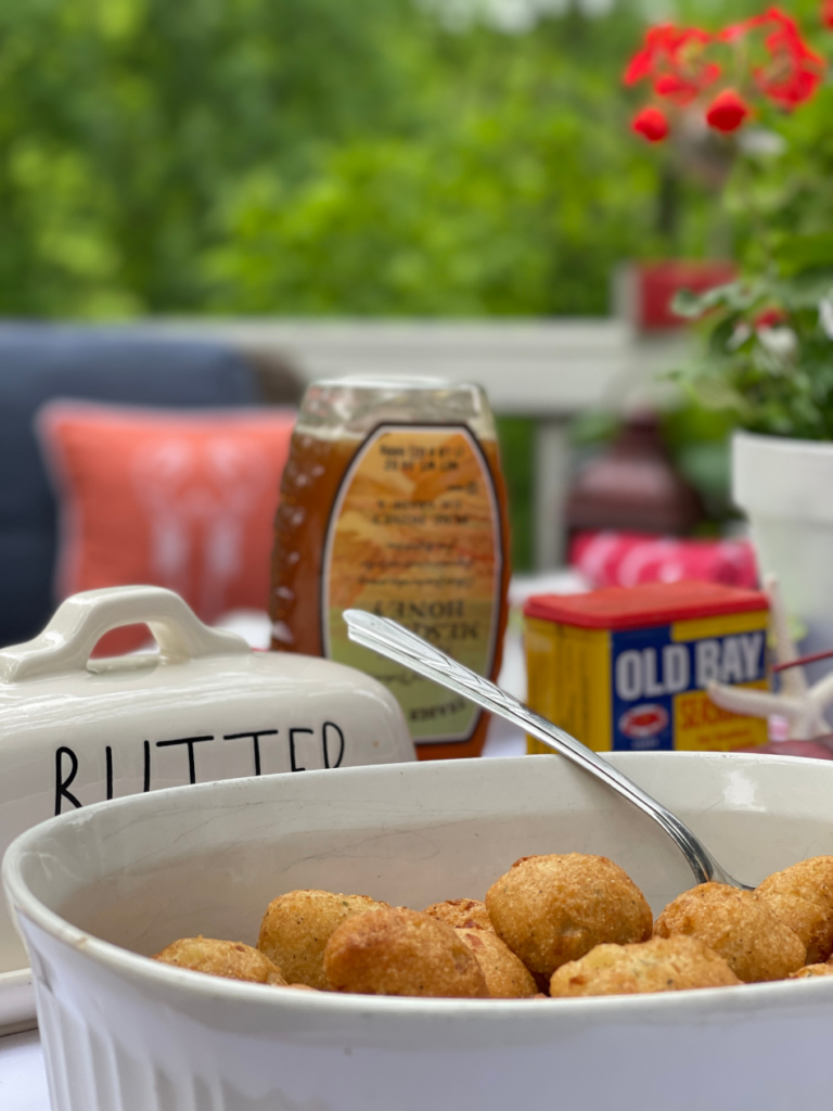 white bowl of hush puppies with old bay seasoning and botttle of honey in background