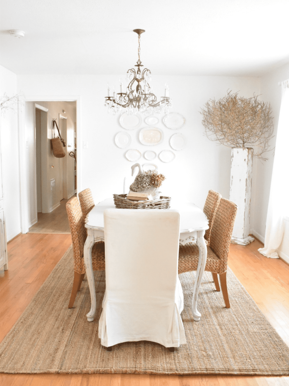 cottage style dining room white slipcovered chairs and woven parsons chairs white french provincial style table vintage chandelier sisal rug under table white painted walls