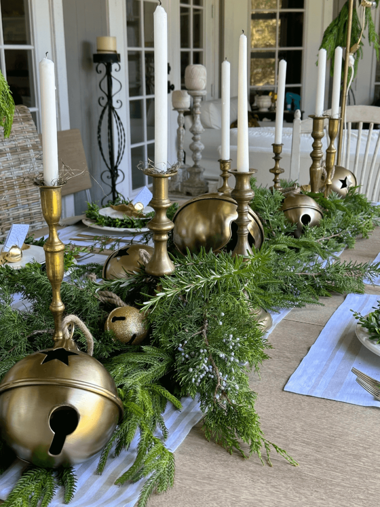 christmas centerpiece white and tan stripe tablerunner fresh and faux greenery down center of table large gold bells and brass candlesticks along table runner and greenery