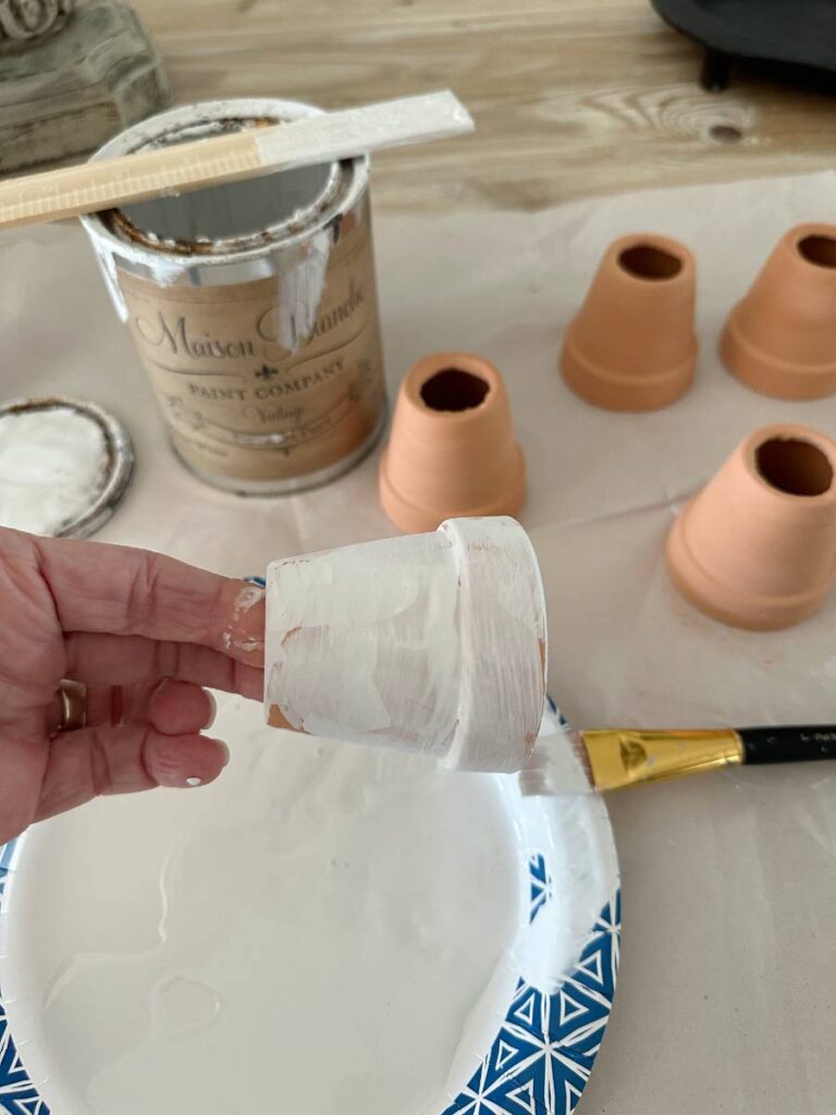 small terra cotta pot being painted white to make into a napkin ring